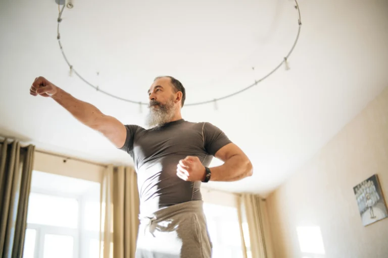 Older bearded man in athletic wear shadow boxing at home, illustrating the energy and vitality men researching testosterone cypionate vs enanthate are often hoping to restore.
