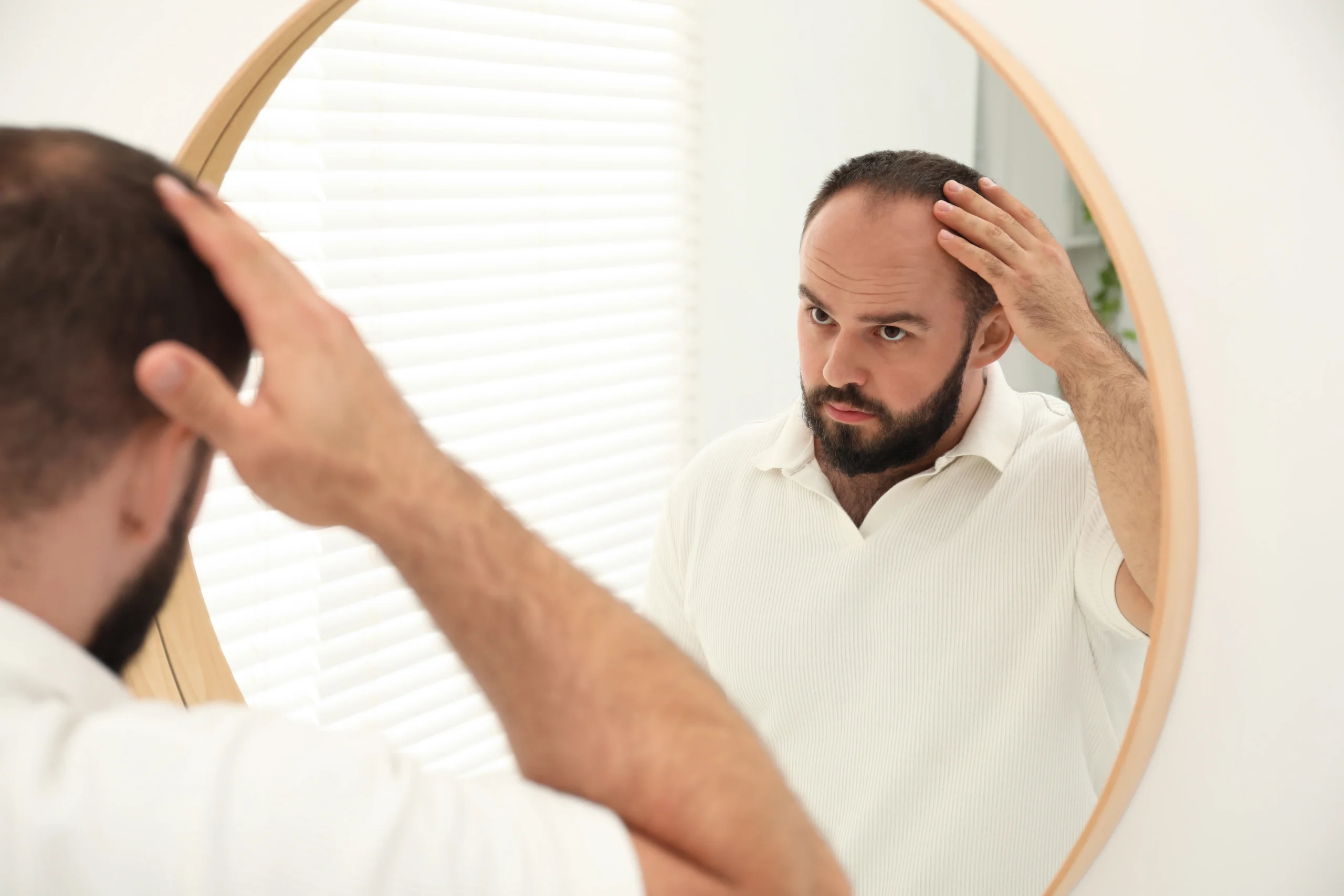 A man examining his hairline in a bathroom mirror at home