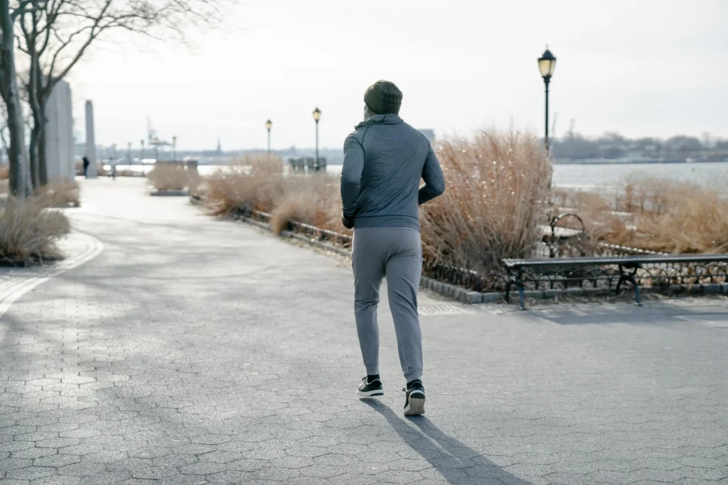 A man jogging along a riverside park path in athletic wear, representing the active lifestyle goals of a GameDay Men's Health treatment plan.