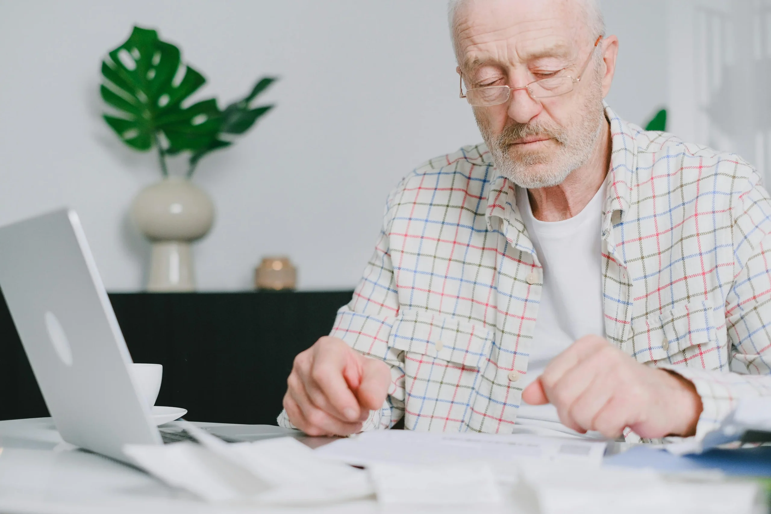 A man reviewing a healthcare bill at his kitchen table with a laptop open, representing the financial planning involved in starting testosterone replacement therapy.