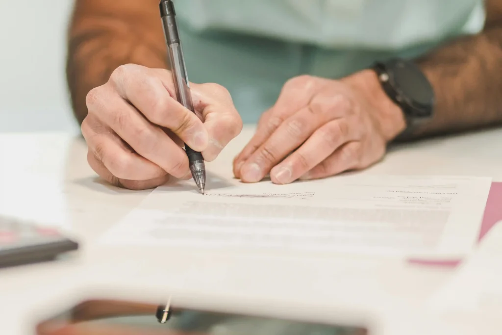 A person signing a medical consultation or membership agreement document with a pen, representing the enrollment process for Hone Health TRT services.