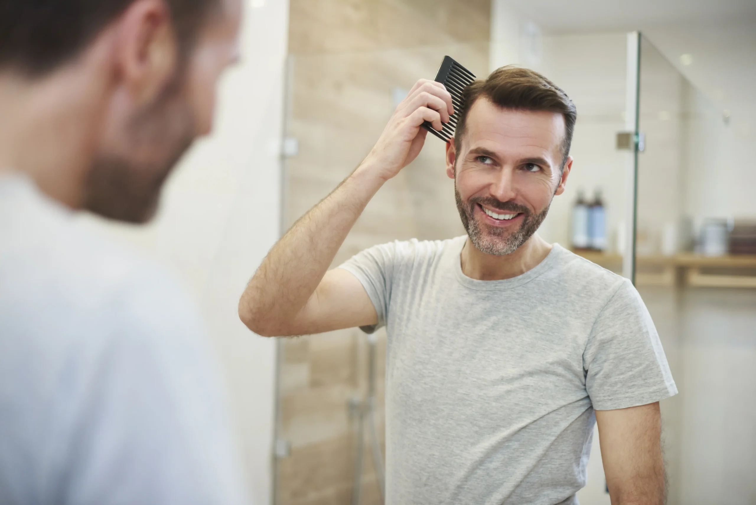 A man combing his hair and looking in a mirror at home