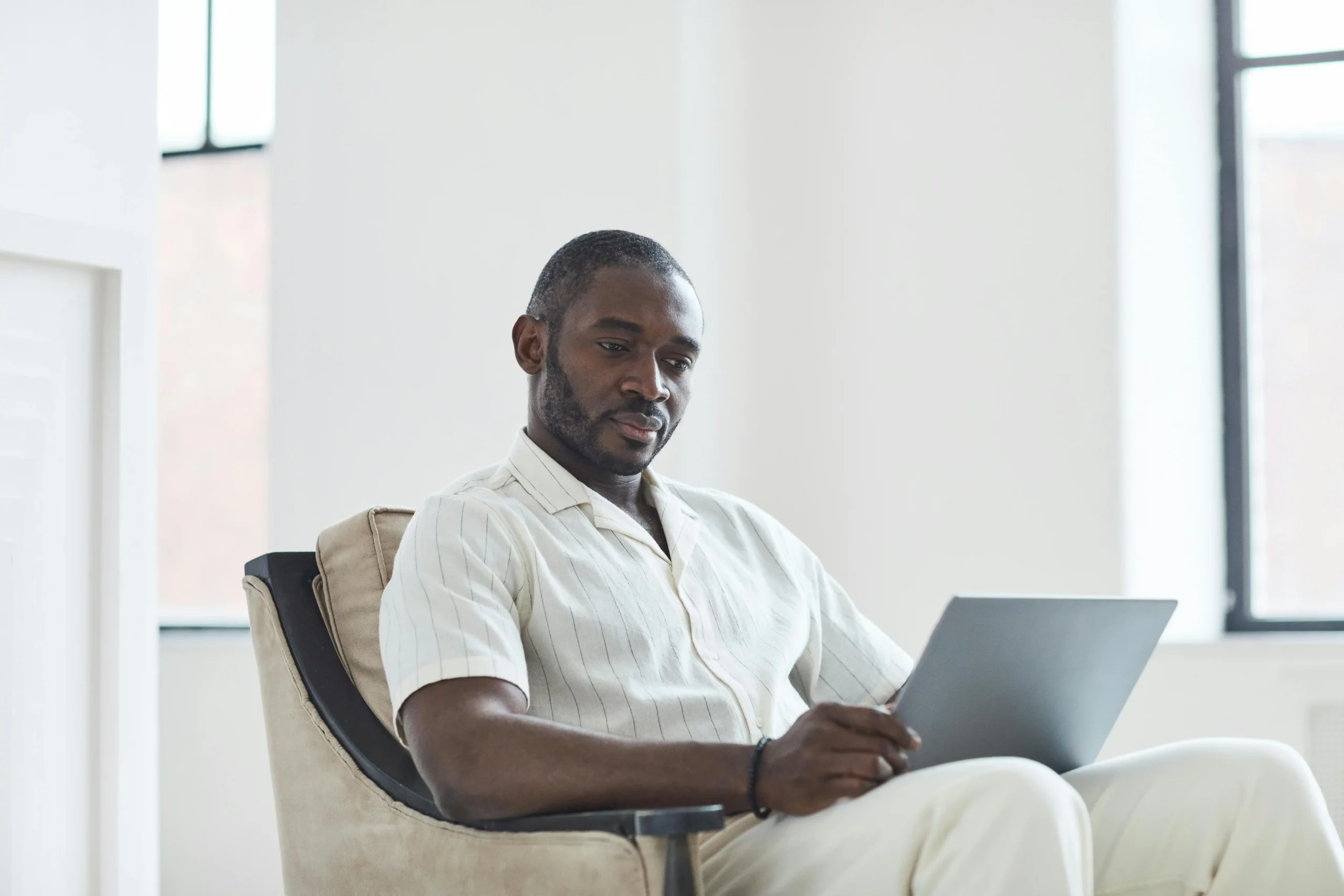 Man in a casual button-down shirt sitting in a modern men's health clinic waiting area, illustrating a review of the GameDay Men's Health franchise TRT experience.