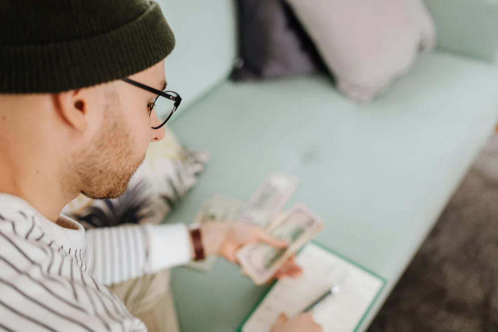 Man reviewing paperwork and counting cash at home while researching Marek Health costs and budgeting for treatment expenses.