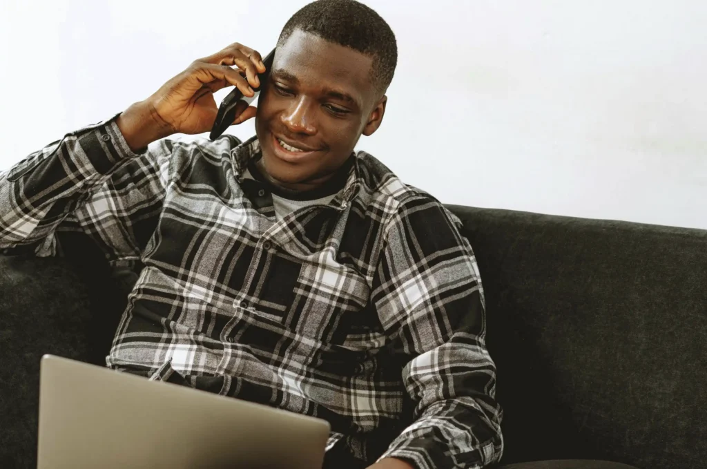 Man using a laptop and talking on the phone at home while researching Maximus TRT and online testosterone replacement therapy services.