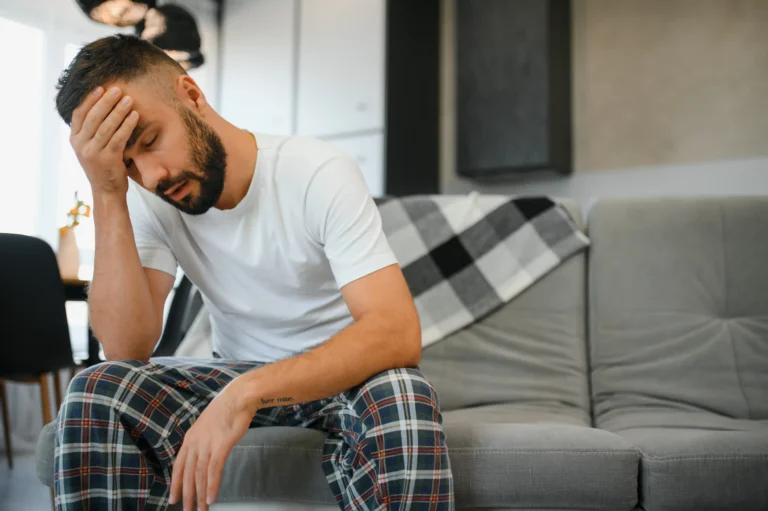A man sitting on a sofa holding his head with a headache