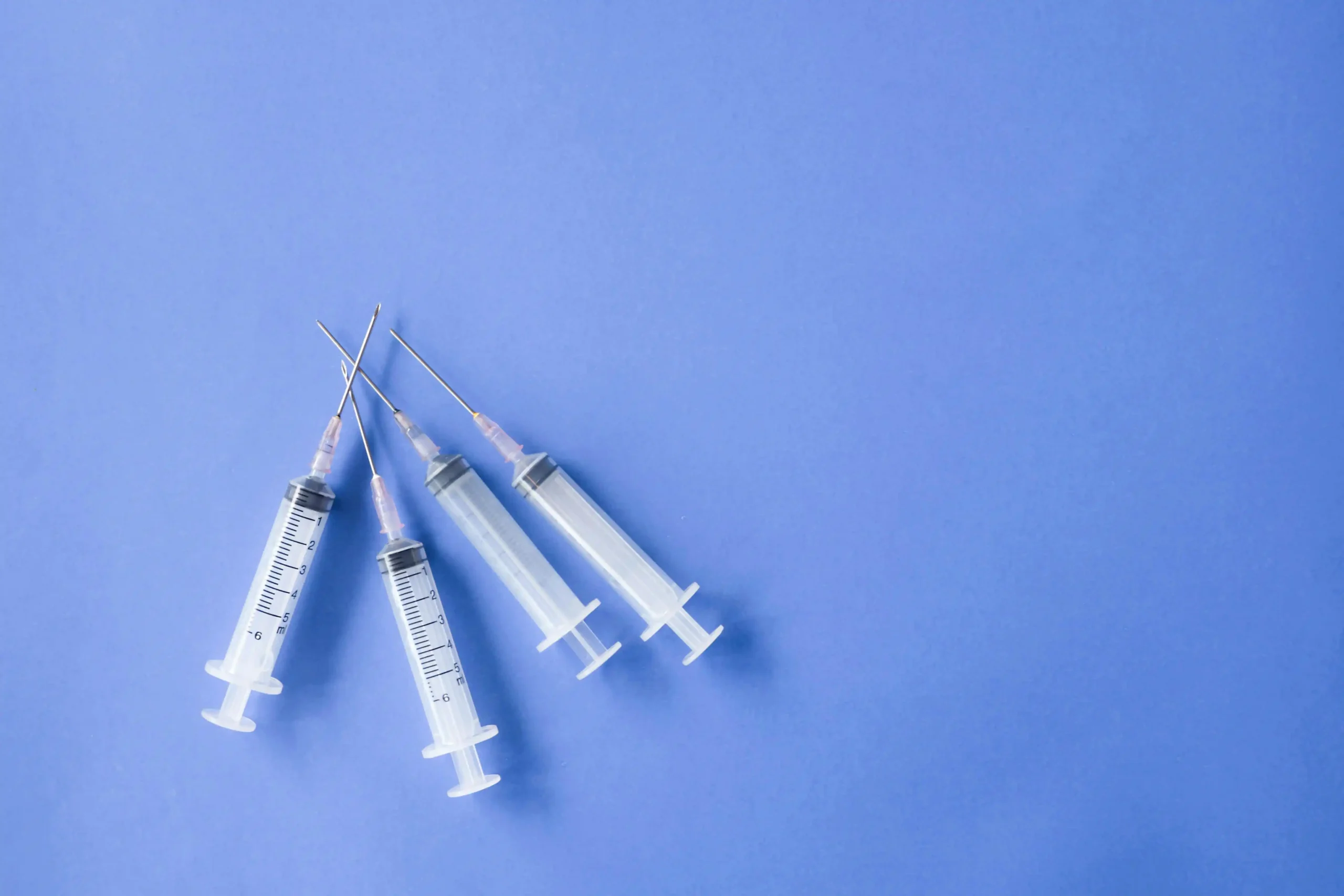 Medical syringes arranged on a blue background for a testosterone injection guide and TRT treatment information.