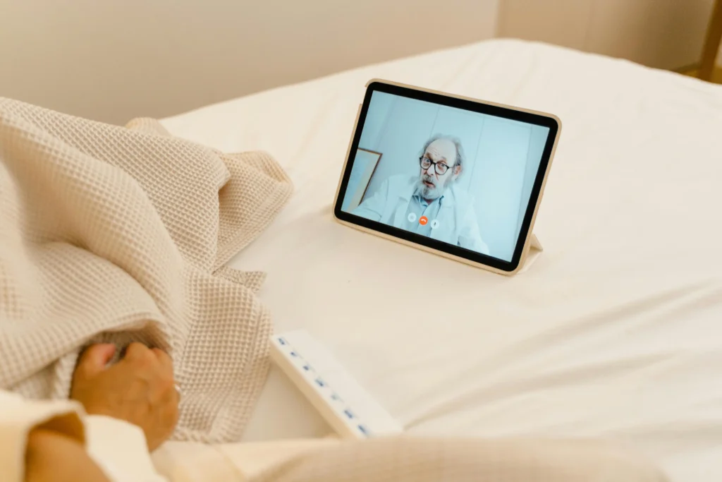 Person attending a virtual doctor consultation on a tablet while resting in bed for an online TRT prescription.