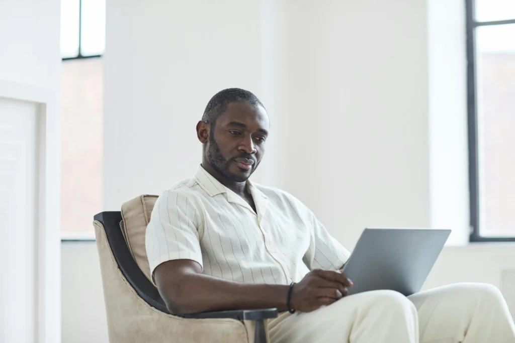 Man in a casual button-down shirt sitting in a modern men's health clinic waiting area, illustrating a review of the GameDay Men's Health franchise TRT experience.