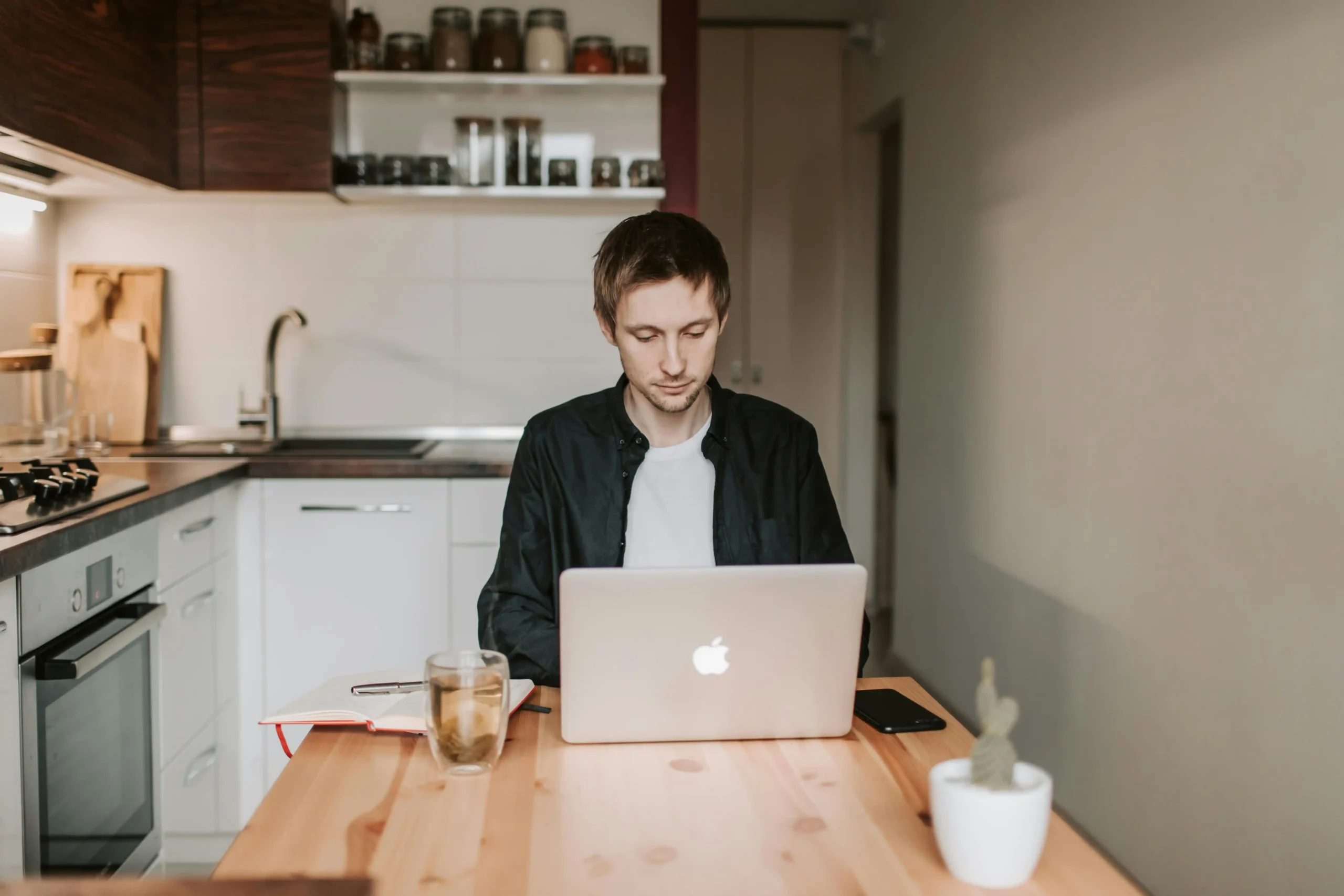 Tired man sitting at his kitchen table reading on a laptop while researching Hone Health TRT options and costs online.