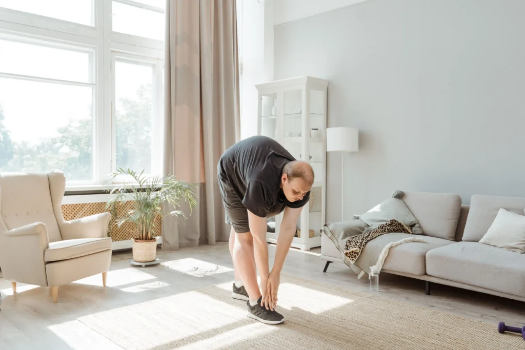 An overweight adult stretches forward to touch their toes while exercising in a bright living room, illustrating a healthy lifestyle and fitness routine often discussed when evaluating the best GLP-1 medication for weight loss, obesity management, and long-term health improvement.