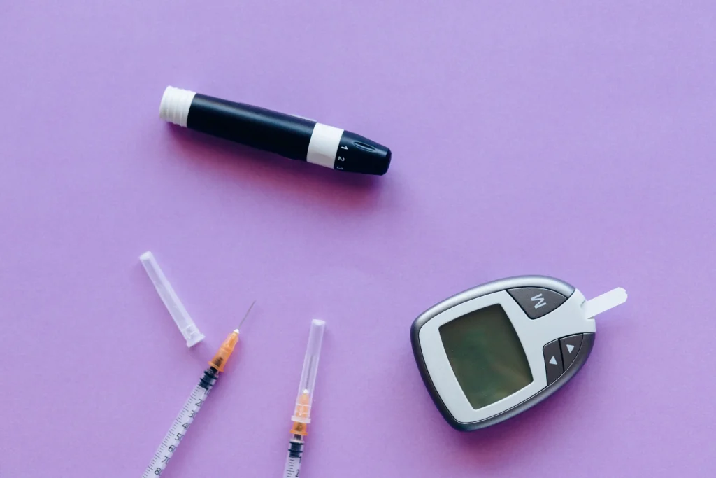 A blood glucose meter, insulin pen, and syringes arranged on a purple background, representing diabetes management and medical weight loss support from the best GLP-1 provider online.