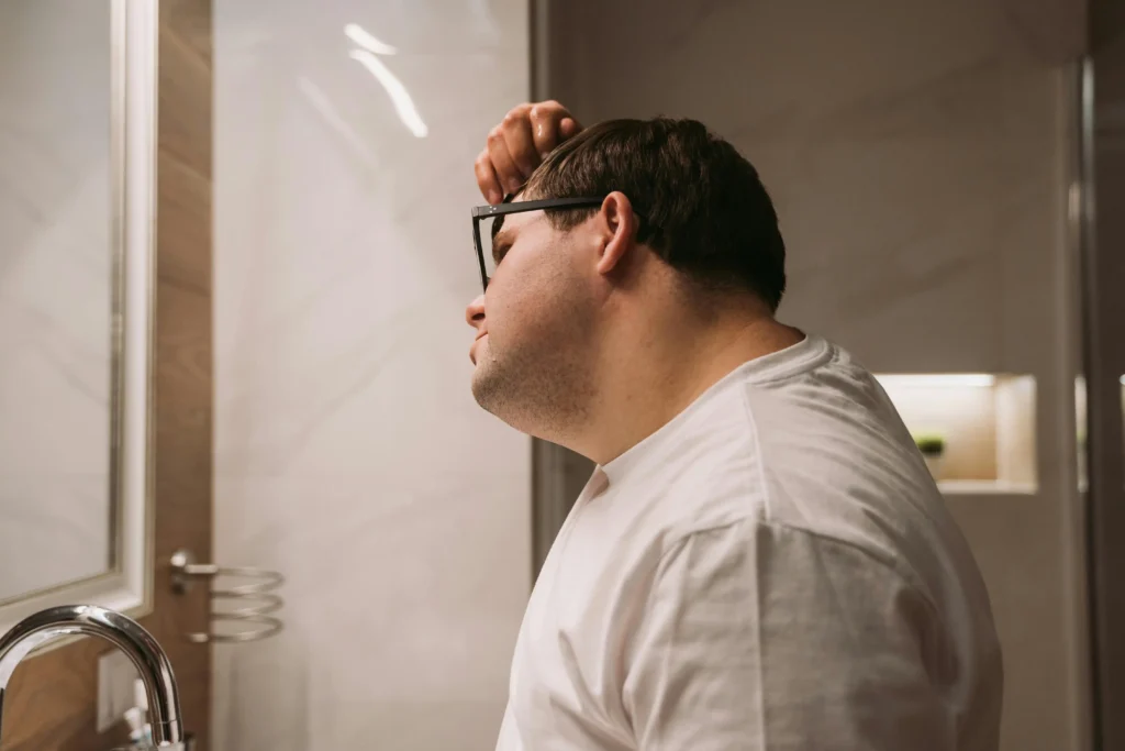 Man looking at his hairline in the mirror, highlighting the search for the best hair loss treatment for men.