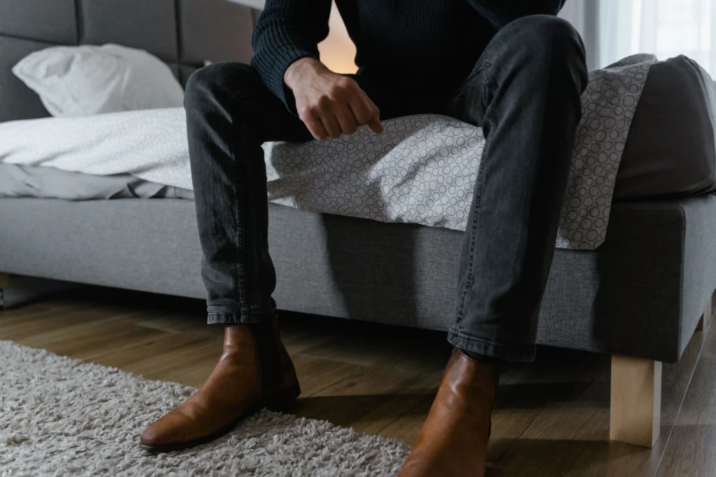 Man sitting on the edge of a bed looking concerned, illustrating common causes of erectile dysfunction and their impact on men's health and wellbeing.