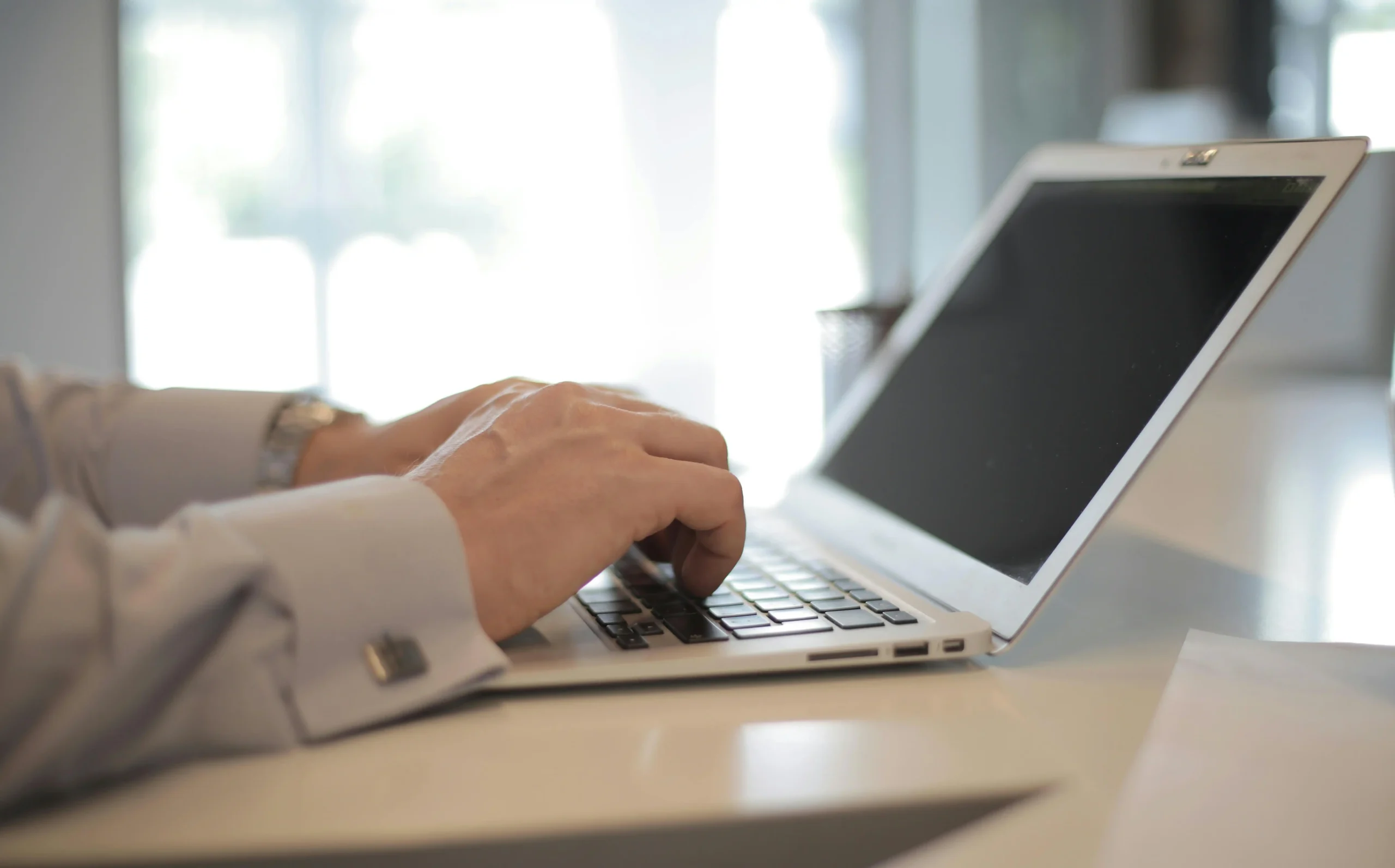 Close-up of a professional typing on a laptop in a bright office setting, representing online research and comparison insights for Maximus vs TRT Nation services.
