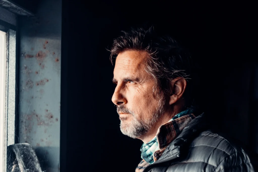 Middle-aged man looking out a window in quiet reflection, representing the question, do I need TRT for low energy and hormonal health?