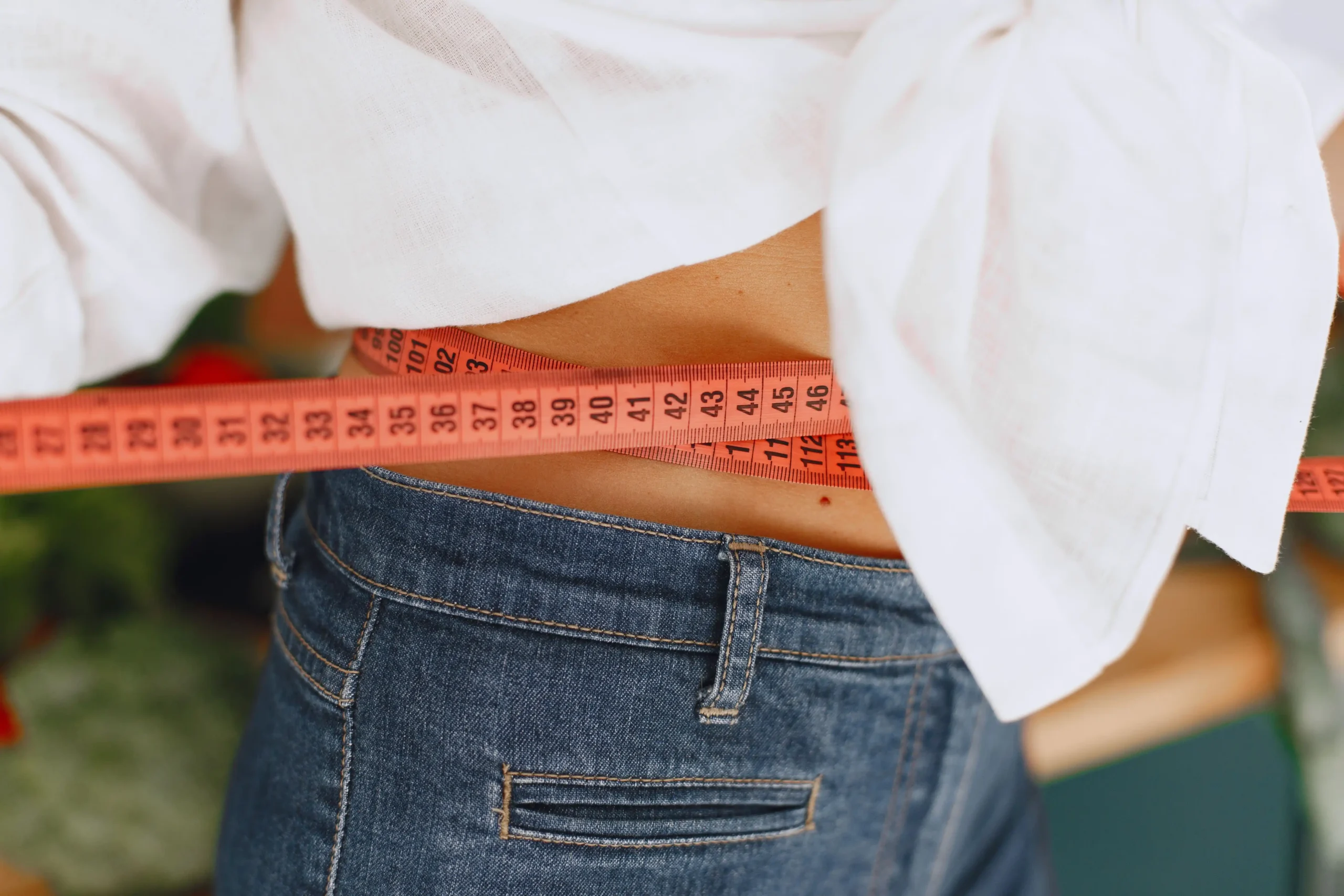 Close-up of a person measuring their waist with a tape measure over jeans, illustrating weight management progress and healthy lifestyle goals discussed in this Henry Meds Review.