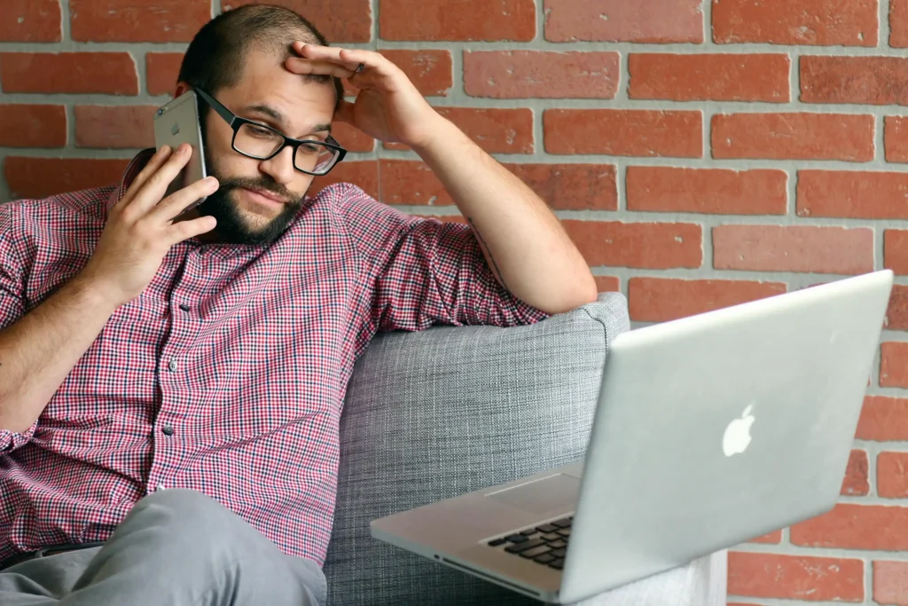 A man with thinning hair looks thoughtfully at his laptop screen while on a phone call, symbolizing a consumer trying to find out is Hims legit for ED.