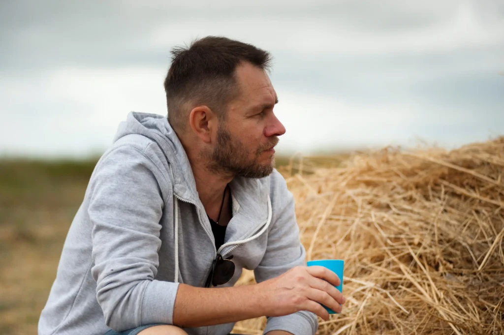 Man sitting outdoors holding a blue cup, reflecting on his health and wellness, representing common signs you need TRT.
