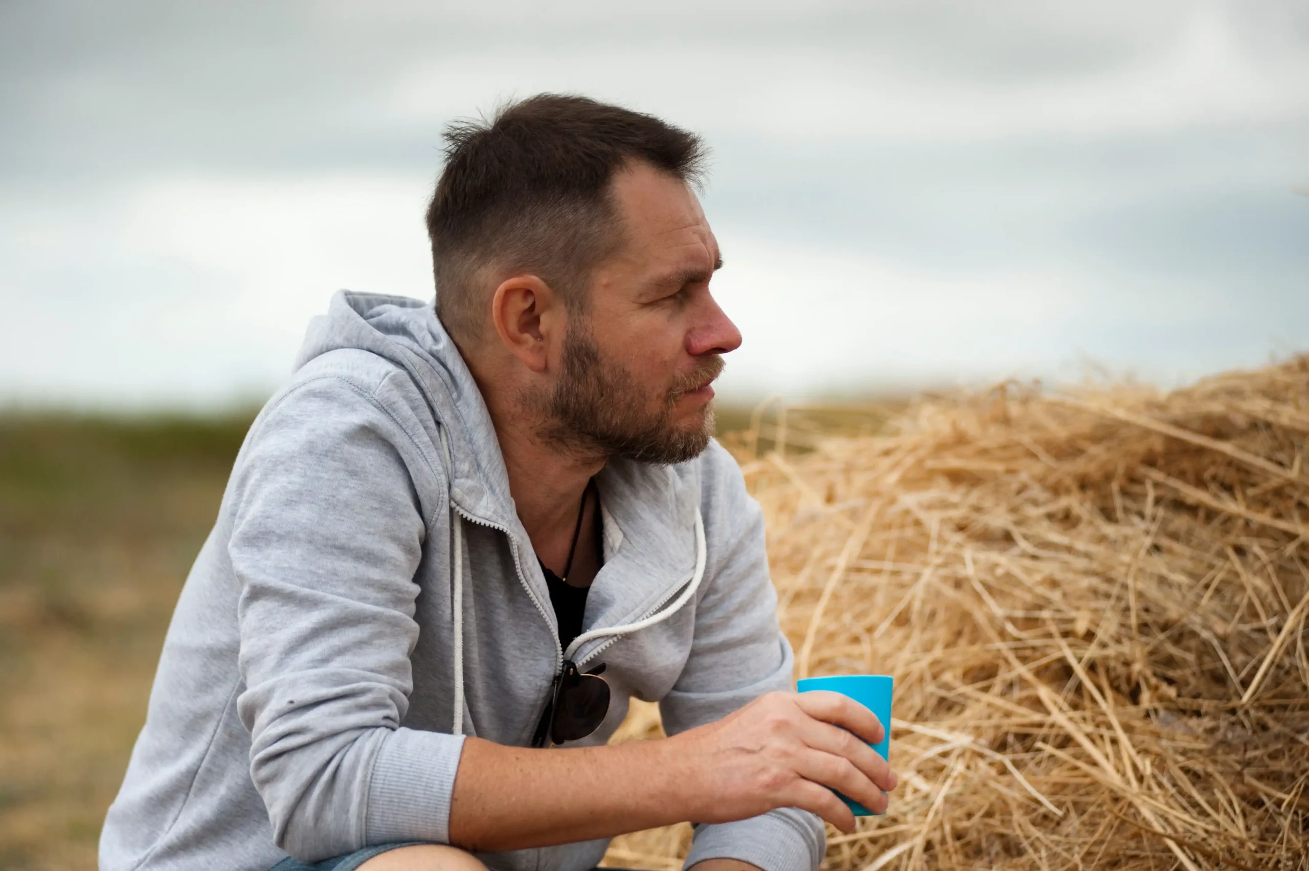 Man sitting outdoors holding a blue cup, reflecting on his health and wellness, representing common signs you need TRT.