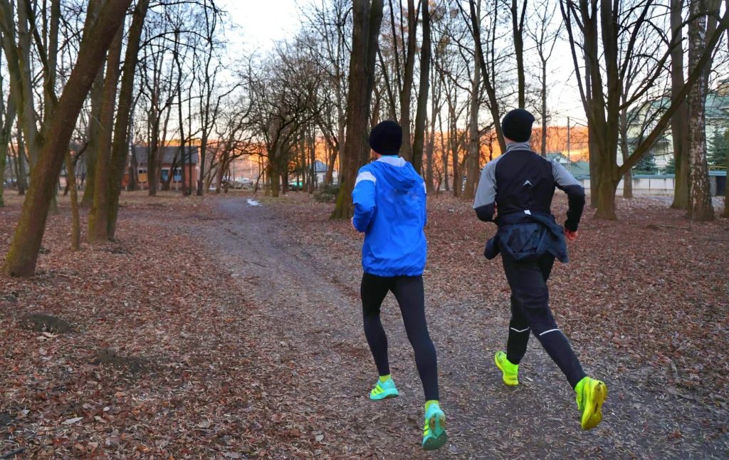 Two runners jogging along a wooded trail during a cool morning, highlighting active lifestyles and fitness outcomes often discussed in Maximus vs TRT Nation comparisons.