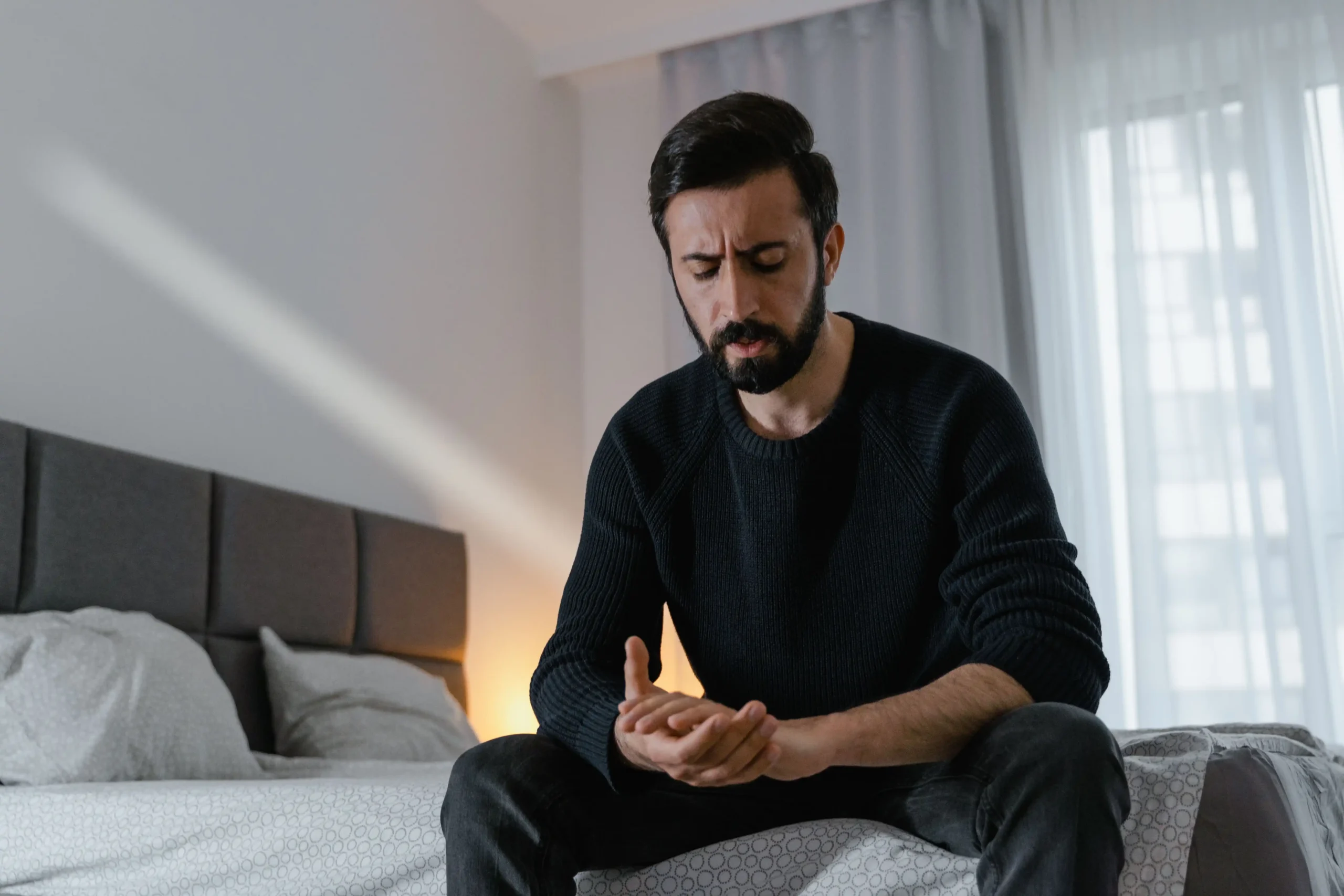 Concerned man sitting on the edge of a bed at night, reflecting the quiet uncertainty many feel when first noticing changes in erectile function.