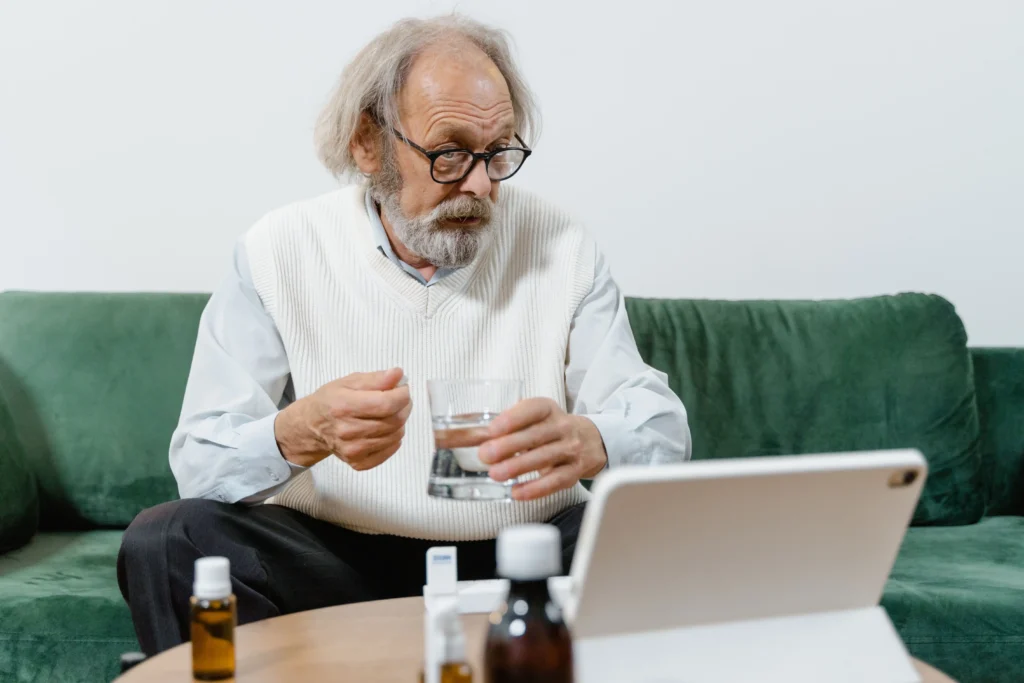 Older man taking medication during a virtual consultation about erectile dysfunction treatment.