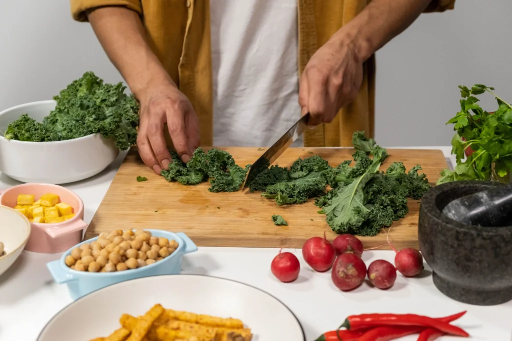 Person preparing a meal with foods that increase testosterone, including leafy greens and chickpeas.