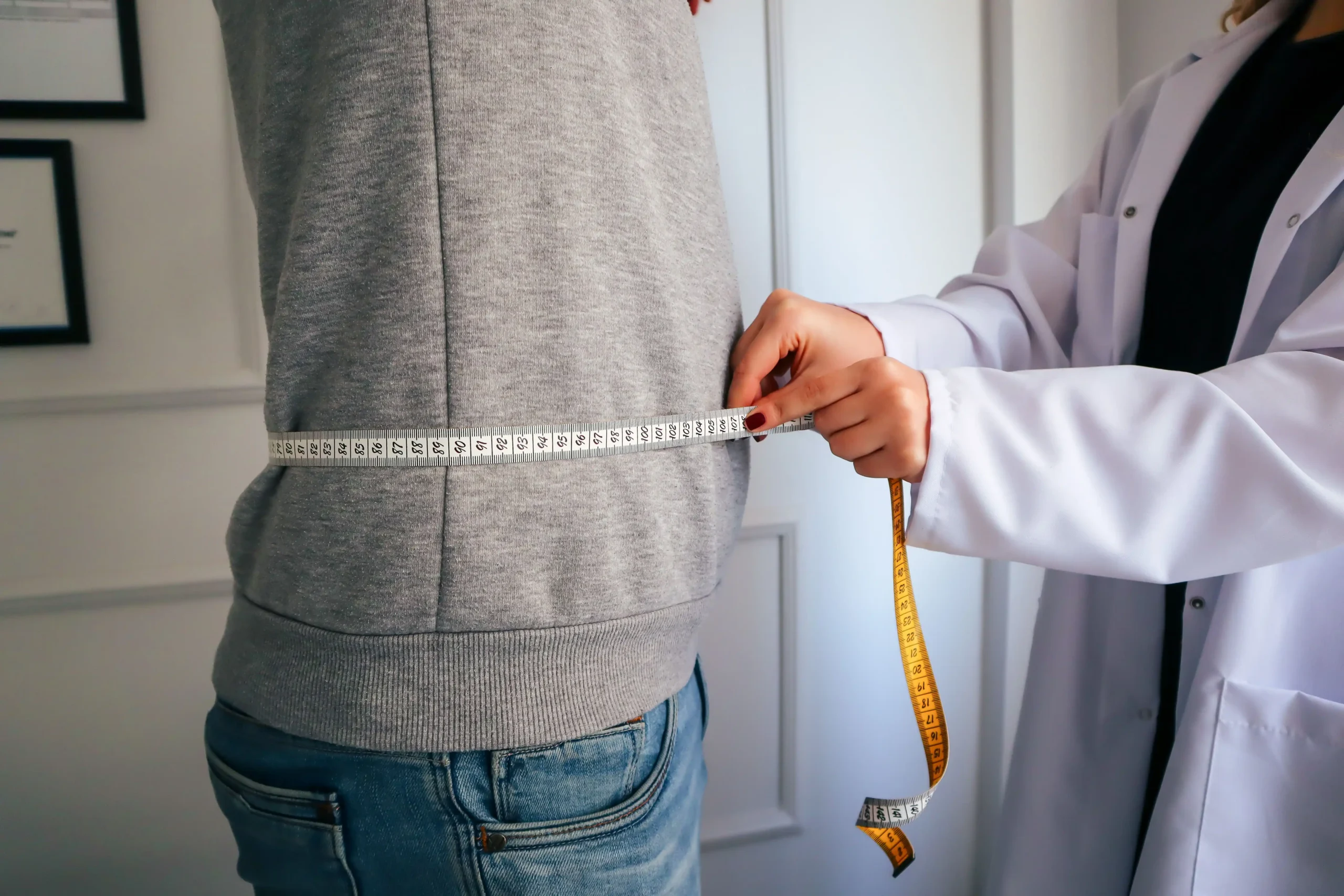 Doctor measuring a patient's waist to track weight loss progress, as discussed in Hims weight loss reviews.