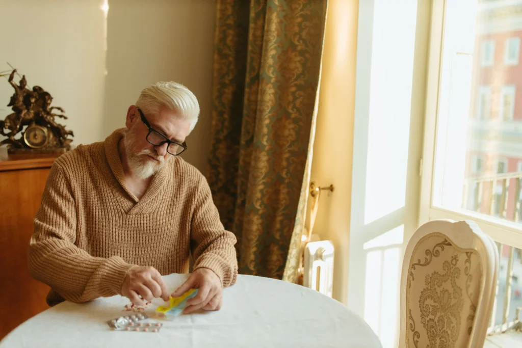 Older man examining pills and medication packaging at a table while researching whether BlueChew is legit.