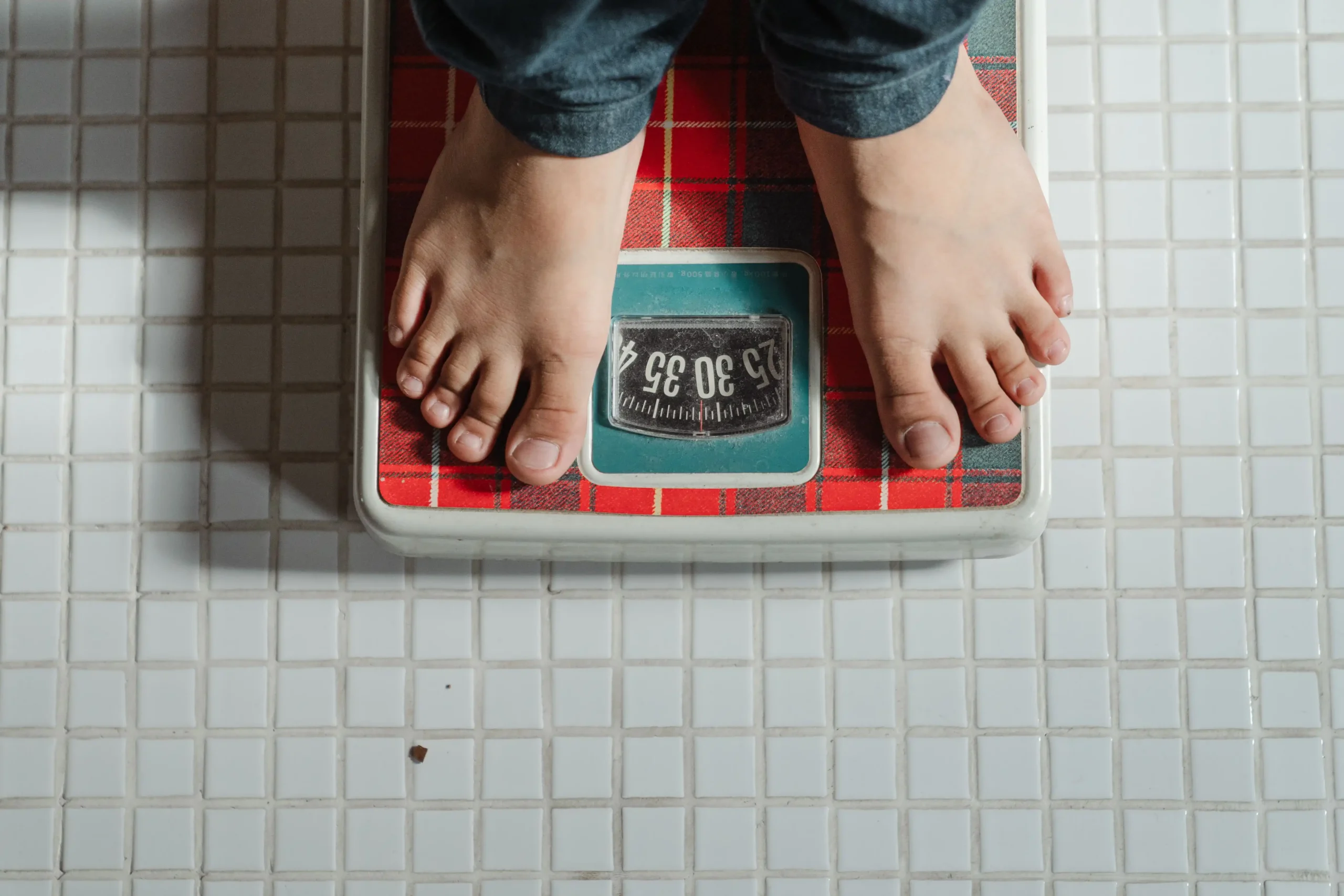 Individual checking their weight on a bathroom scale as part of an online weight loss program.
