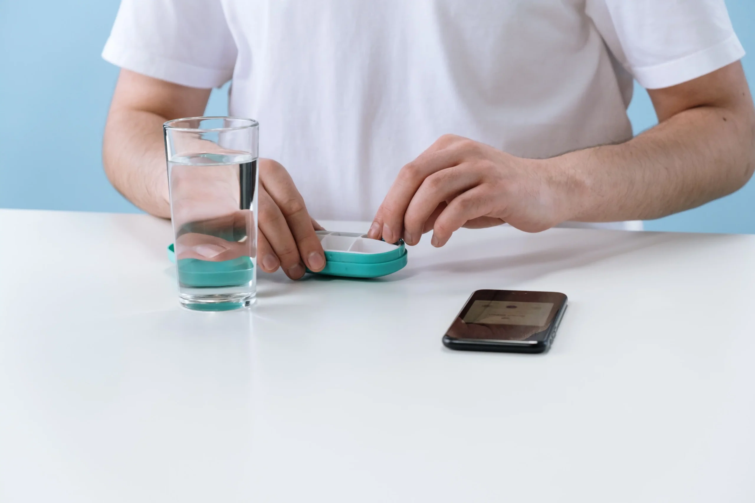 Man handling pills from a weekly pill organizer while considering sildenafil vs tadalafil.