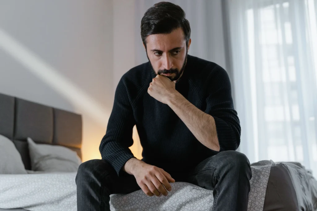 Concerned man sitting on his bed while considering the differences between Viagra vs Cialis.