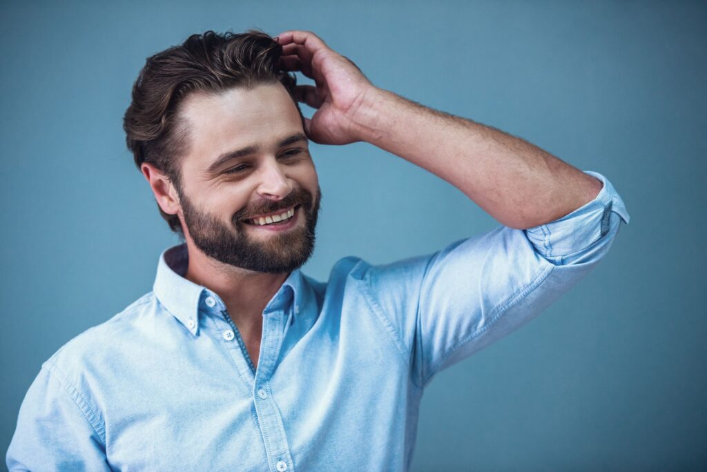 A smiling man with a beard running a hand through his hair
