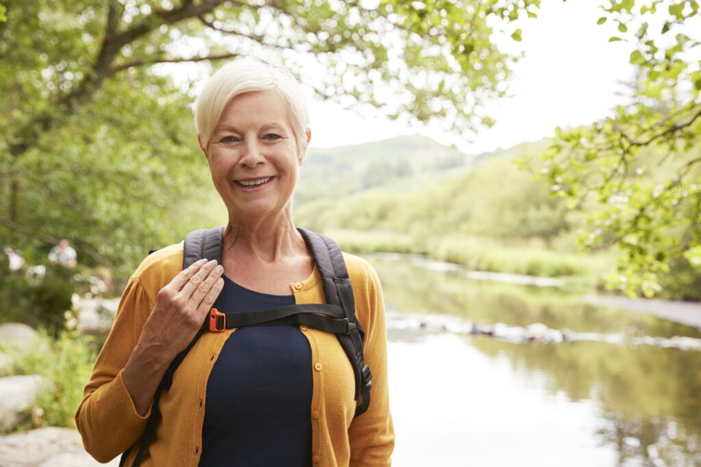 A smiling woman in her sixties hiking beside a river