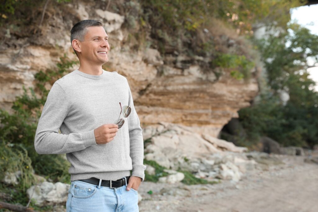 A smiling man in a grey sweater standing outdoors by a cliff path