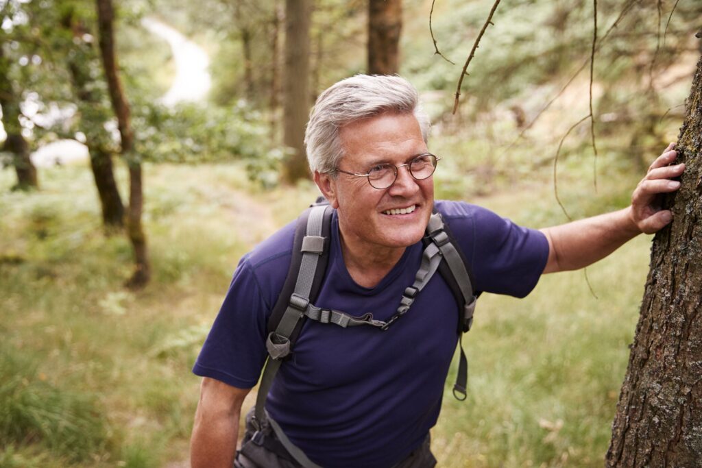 A smiling man in his sixties hiking on a forest trail