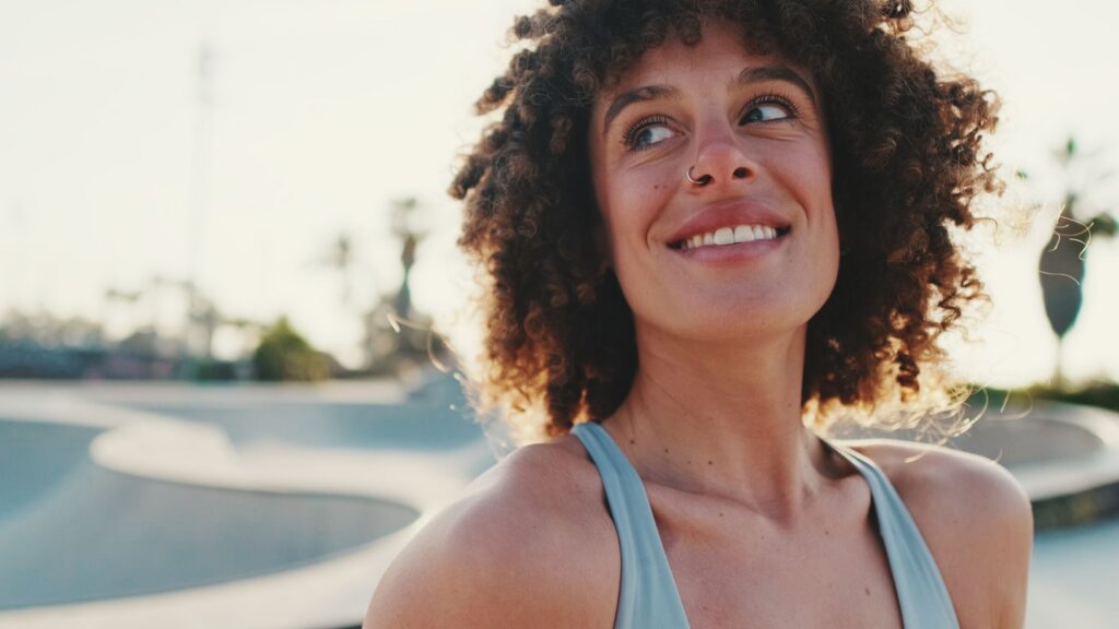 A smiling woman with curly hair outdoors in the sun